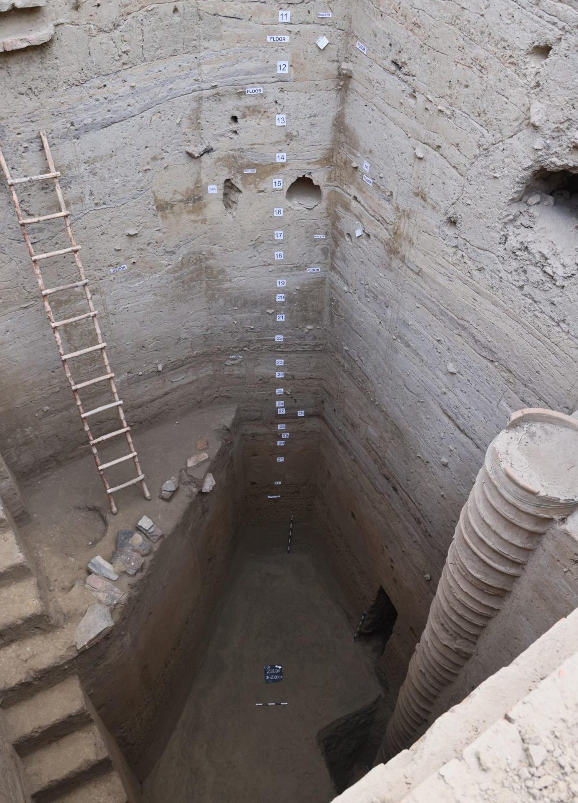 A deep excavation trench at Bahaj cut through many metres of stratified soil, a ladder standing in it for scale