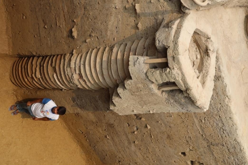 An excavator beside a tall stack of terracotta ring-well rings